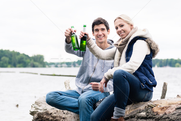 couple sitting on tree stump at the riverside drinking beer  Stock photo © Kzenon