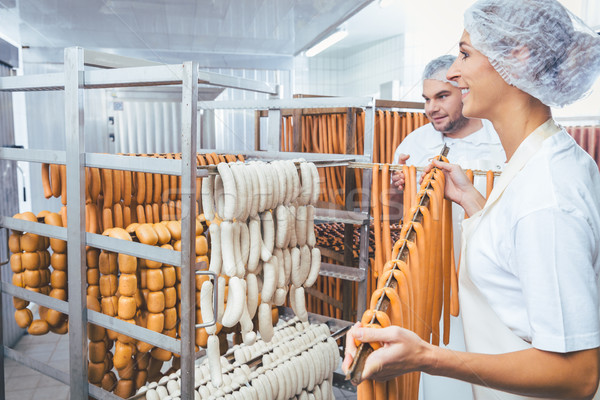 Woman working in butchery putting sausages on beam in rack Stock photo © Kzenon