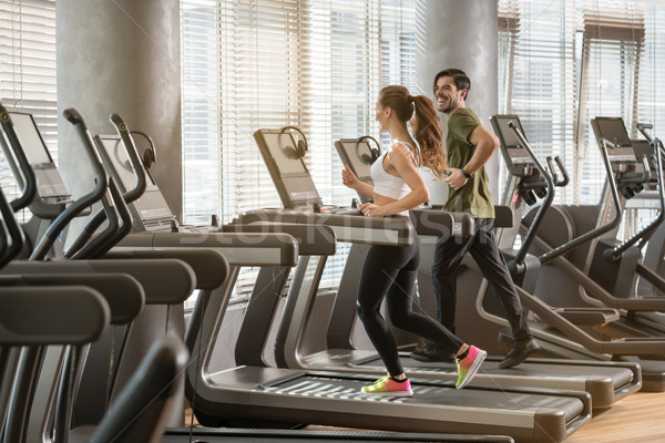 Stock photo: Young man and woman smiling while running side by side on treadmill