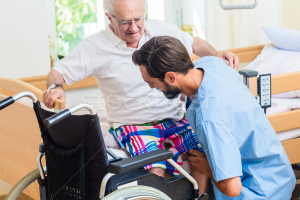 Elderly care nurse helping senior from wheel chair to bed Stock photo © Kzenon