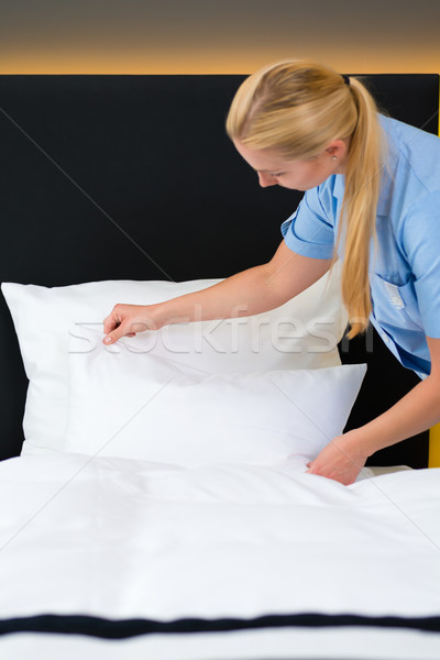 Service in hotel, maid puts clean sheets on bed Stock photo © Kzenon