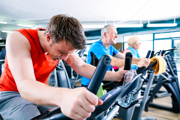 Sport in the gym - people spinning of fitness bikes Stock photo © Kzenon