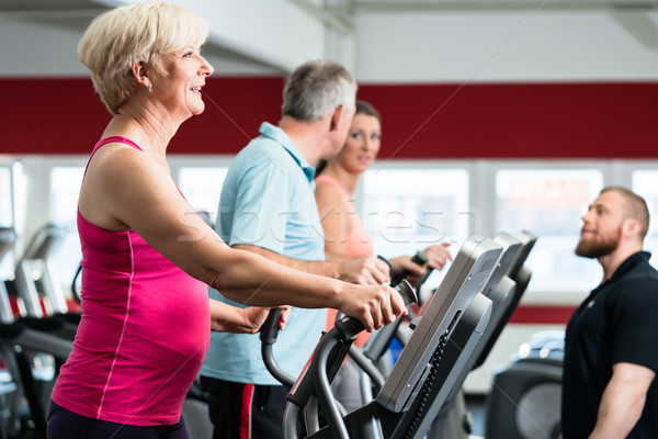 Seniors training on cross trainer with personal trainer at the g Stock photo © Kzenon