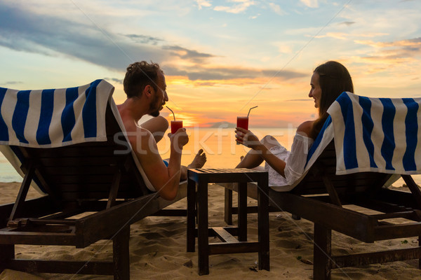 Young couple drinking cocktails on a beach at sunset during vacation Stock photo © Kzenon
