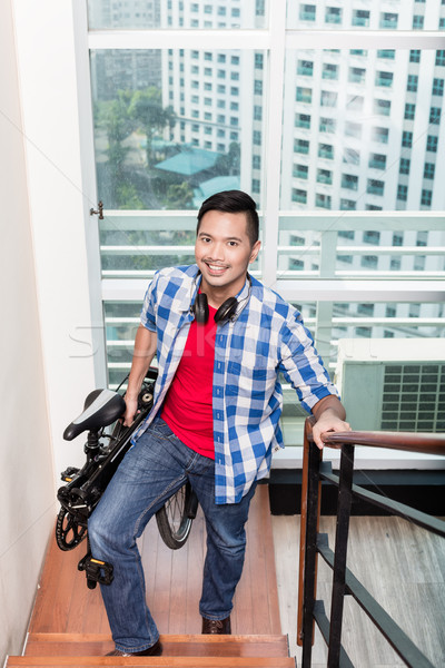 Young asian man carrying folding bike up the stairs to apartment Stock photo © Kzenon