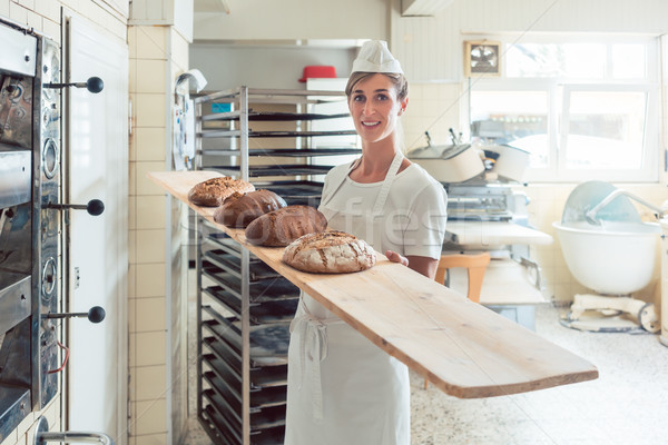Baker woman presenting bread on board in bakery Stock photo © Kzenon