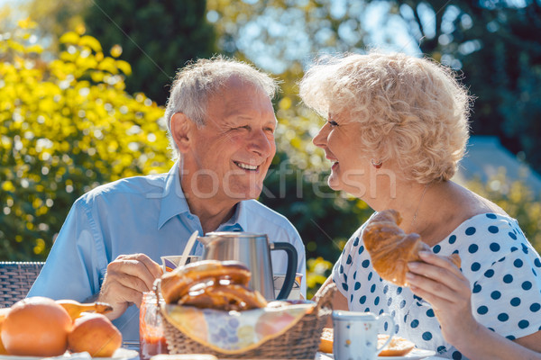Happy elderly couple eating breakfast in their garden outdoors Stock photo © Kzenon