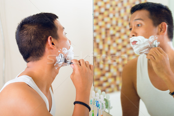 Asian man shaving in front of mirror Stock photo © Kzenon