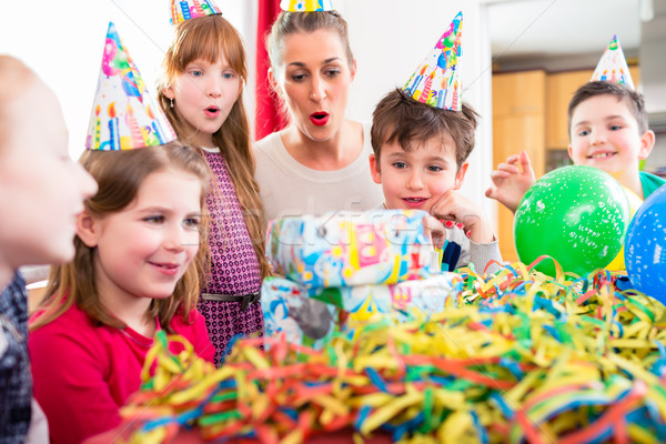 Stock photo: Child unwrapping birthday gift with friends