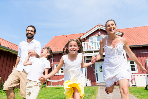 Happy family running on meadow in front of house Stock photo © Kzenon