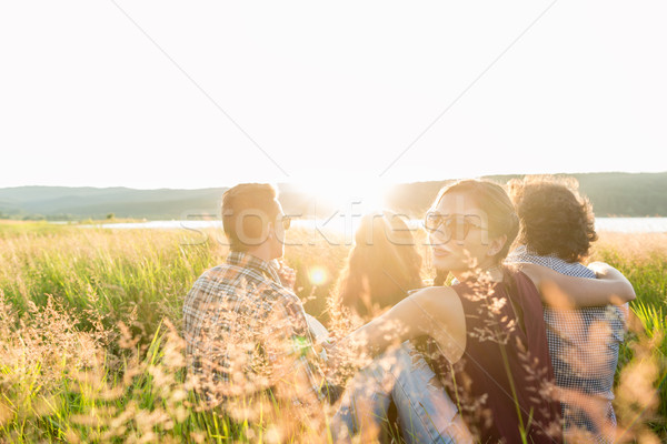 Friends sitting together at lake enjoying sunset Stock photo © Kzenon