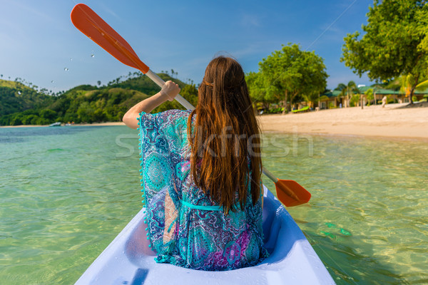 Young woman paddling a canoe along the shore of an idyllic islan Stock photo © Kzenon