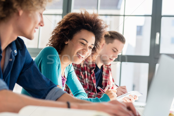 Cheerful woman writing an assignment while sitting between two classmates Stock photo © Kzenon