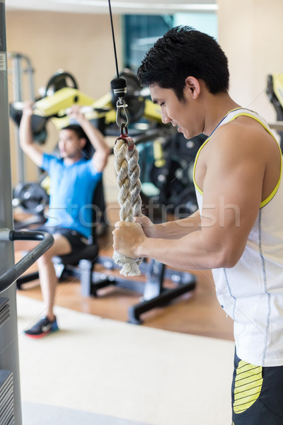 Strong young man exercising triceps pushdown at the rope cable machine Stock photo © Kzenon