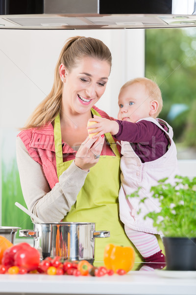 Mother working in kitchen while carrying child Stock photo © Kzenon