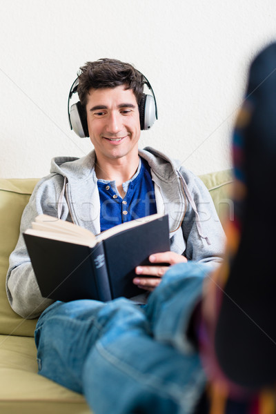 Relaxed young man lying down on the couch while reading a book a Stock photo © Kzenon