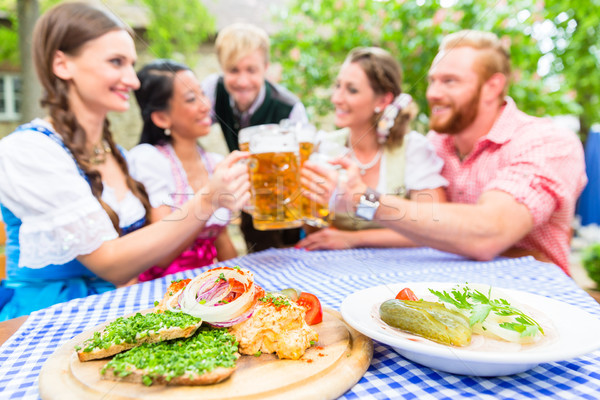Friends in beer garden with drink and Bavarian appetizers Stock photo © Kzenon