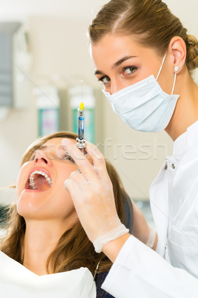 dentist holding a syringe and anesthetizing her patient Stock photo © Kzenon