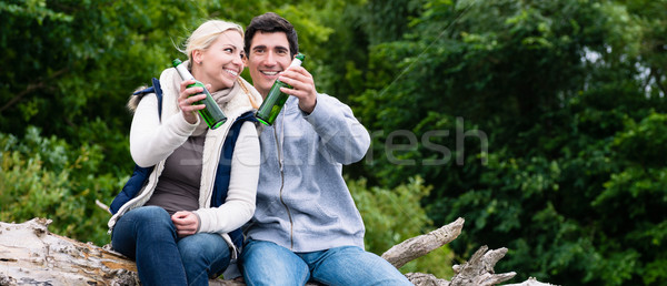 Stock photo: Lovers in vacation sitting at waterside clinking beer bottles