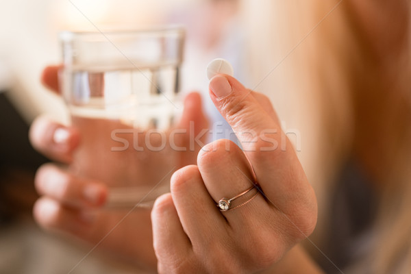Hands of a woman holding a pill and a glass of water Stock photo © Kzenon