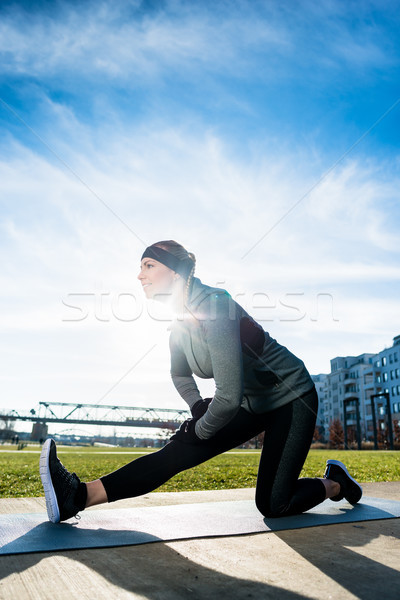 Determined young woman stretching her leg while kneeling on a ma Stock photo © Kzenon
