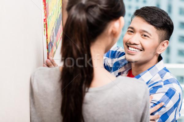 Young asian couple hanging up picture paintings Stock photo © Kzenon
