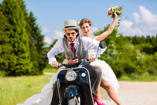 Bridal pair driving motor scooter wearing gown and suit Stock photo © Kzenon