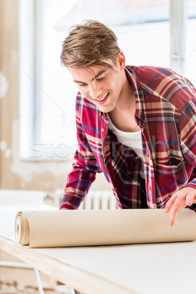 Young man applying paste to the surface of a wallpaper sheet dur Stock photo © Kzenon