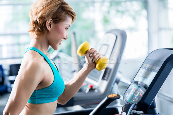 Asian woman walking on treadmill holding dumbbell Stock photo © Kzenon