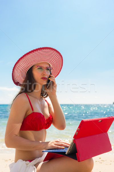 Fashionable young woman talking on mobile phone and using a tablet on the beach Stock photo © Kzenon