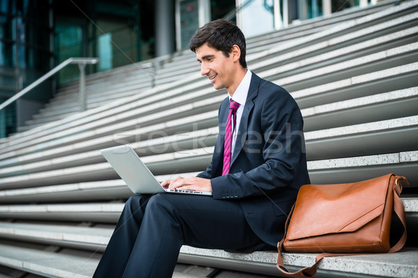 Young businessman using a laptop while sitting down outdoors  Stock photo © Kzenon