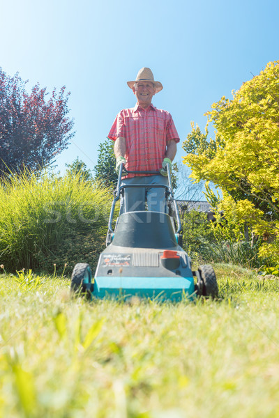 Active senior man smiling while using a grass cutting machine in the garden Stock photo © Kzenon