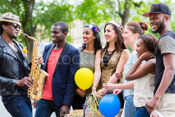 Street artist playing saxophone for multi-ethnic party group  Stock photo © Kzenon