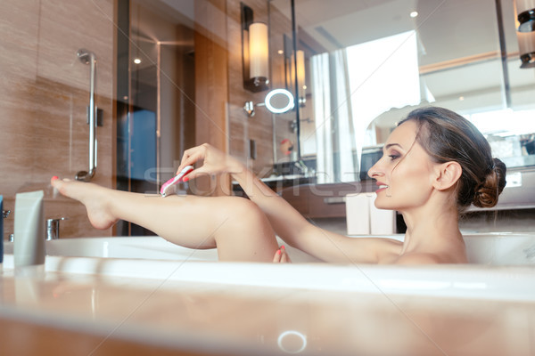 Woman having bath in hotel bathtub grabbing her shaver Stock photo © Kzenon