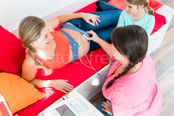 Stock photo: Young girl watching midwife attaching CTG to pregnant belly of m