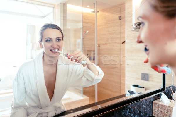 Woman brushing her teeth in luxurious hotel looking at herself Stock photo © Kzenon