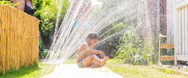 Boy cooling down with garden hose, family in the background Stock photo © Kzenon