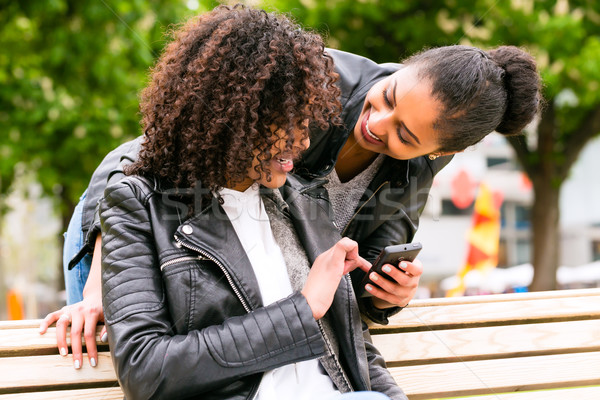 Best friends chatting with smartphone on park bench Stock photo © Kzenon