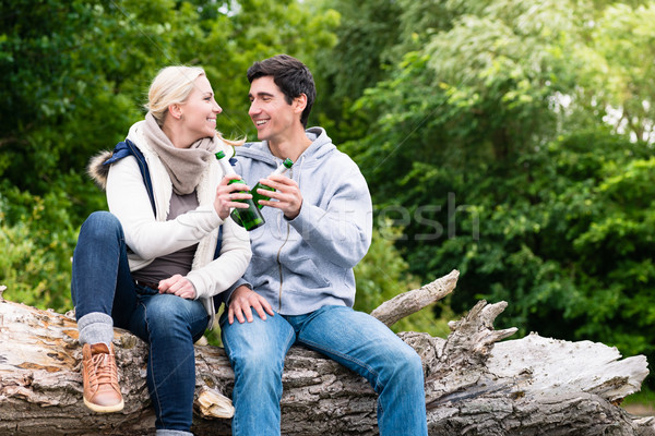 Lovers in vacation sitting at waterside clinking beer bottles Stock photo © Kzenon