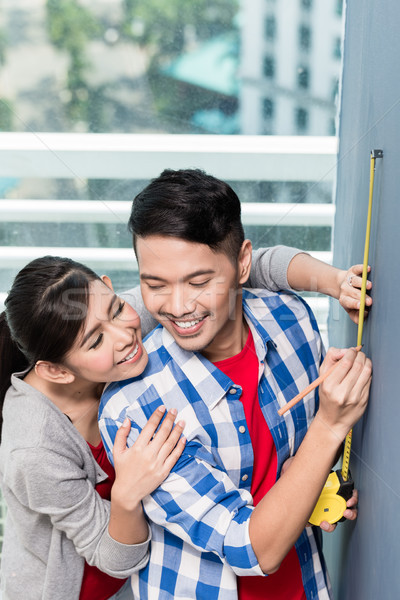 Young indonesian couple measuring walls in new apartment Stock photo © Kzenon