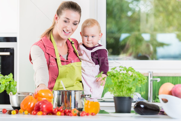 Mother working in kitchen while carrying child Stock photo © Kzenon