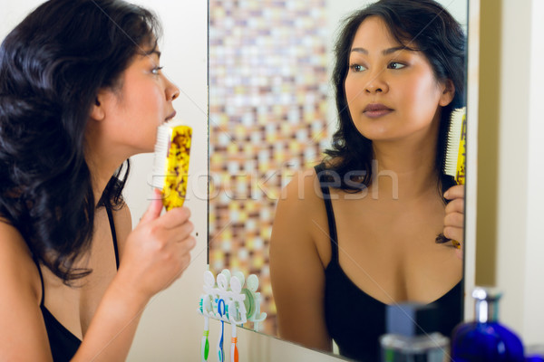 Asian woman combing hair in bathroom mirror Stock photo © Kzenon