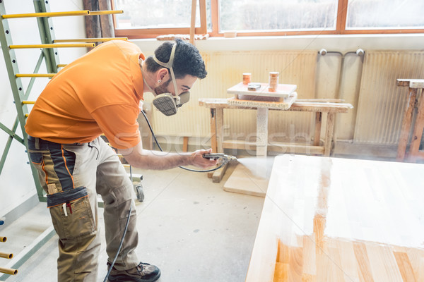 carpenter man spraying varnish on a table he works on Stock photo © Kzenon