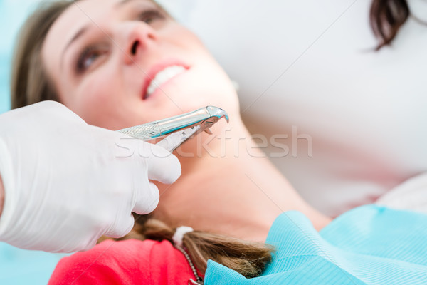 Dentist extracting tooth of woman with extractor Stock photo © Kzenon