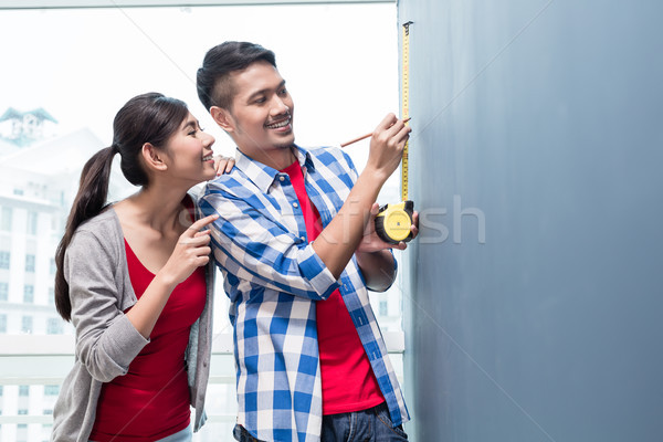 Young indonesian couple measuring walls in new apartment Stock photo © Kzenon