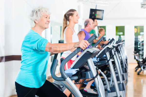 Group of people on elliptical trainer exercising in gym Stock photo © Kzenon