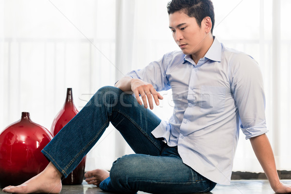 Lehangolt ázsiai férfi ül lakás padló Stock fotó © Kzenon