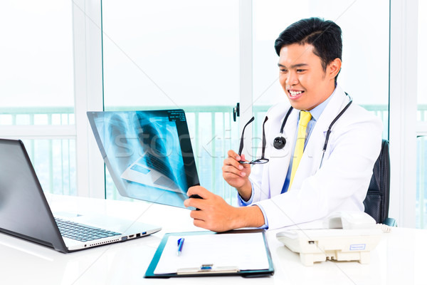 Asian doctor examining x-ray picture in practise Stock photo © Kzenon