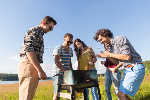 Young people having barbecue on field near lake Stock photo © Kzenon
