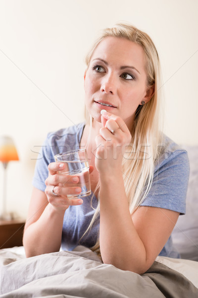 Young woman sitting in bed taking a tablet Stock photo © Kzenon